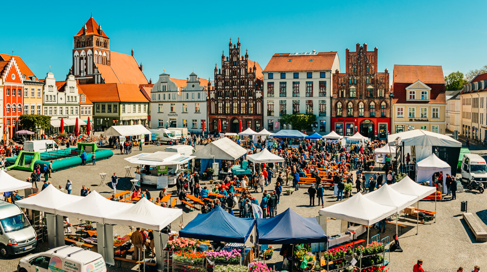 Greifswalder Marktplatz von oben mit vielen Pavillons, Autos und Menschen