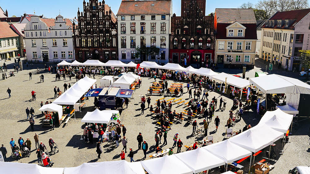 Der Greifswalder Marktplatz mit vielen Pavillons, Menschen und Transportwagen
