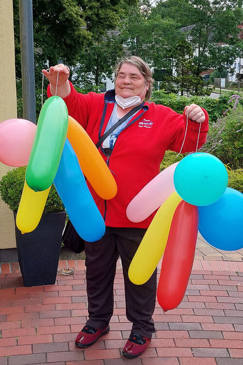 Eine Frau hält links und rechts jeweils ein Bündel mit aufgeblasenen Luftballons