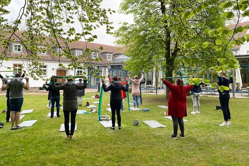 Eine Gruppe steht in einem Garten und macht Sportübungen mit einer Matte