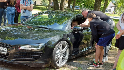 Eine Junge und ein Mann stehen an der Tür eines Sportwagens und sprechen mit dem Fahrer.