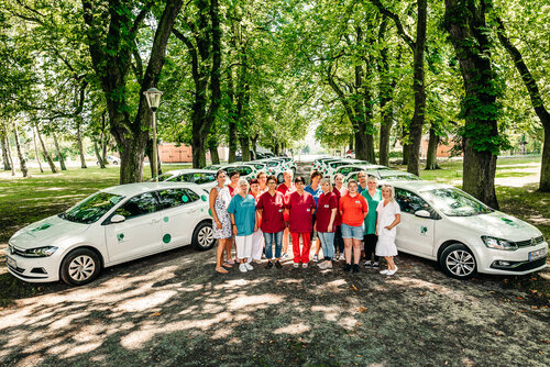 200122 Mitarbeitende Pflegedienste Griebenow Mitarbeiterinnen stehen zwischen ihren Dienstfahrzeugen auf einer Allee unter Bäumen