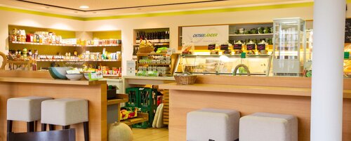 Blick in den Gastraum des Hofladens mit gefüllten Produktregalen und gepolsterten Sitzhockern