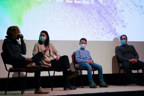 Eine Frau und ein Mann sprechen miteinander, rechts daneben sitzt ein Junge und ein Mann