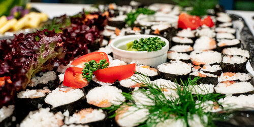 Sushiröllchen liegen mit Tomaten und Dill verziert auf einer Platte auf einem Buffet