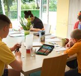 Eine Erzieherin sitzt mit drei Kindern und Jugendlichen an einem Tisch und bearbeitet Aufgaben