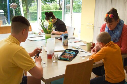 Eine Erzieherin sitzt mit drei Kindern und Jugendlichen an einem Tisch und bearbeitet Aufgaben