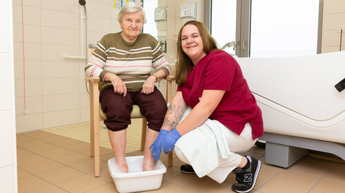 Ausbildung im Pommerschen Diakonieverein Eine ältere Dame hat ihre Füße in eine Plastikschale gestellt, um ein Fußbad von einer jüngeren Frau zu bekommen