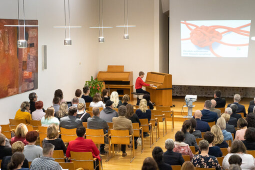 Ein Junge sitzt in einem großen Saal am Klavier und viele Leute hören ihm zu