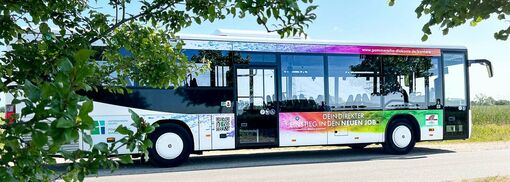 Ein bedruckter Bus mit Werbeaufschrift fährt durch die Landschaft