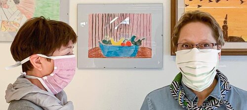 Zwei Frauen, deren Mund und Nase mit Stoffmasken bedeckt ist.