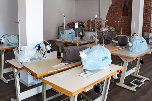 In einem großen Raum stehen mehrere Tische mit Nähmaschinen, die in Schutzhüllen gepackt sind