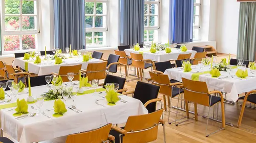 Ein großer Festsaal mit feierlich gedeckten Tischen, Servietten, Tischdecken und Geschirr