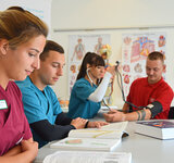 Junge Menschen in Arbeitskleidung sitzen um einen großen Konferenztisch