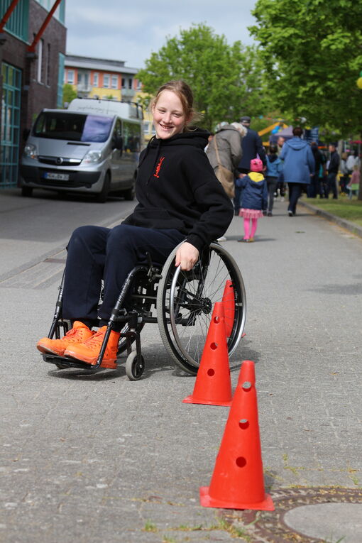 Eine Rollstuhlfahrerin fährt um Hütchen, die auf einer Straße aufgestellt sind