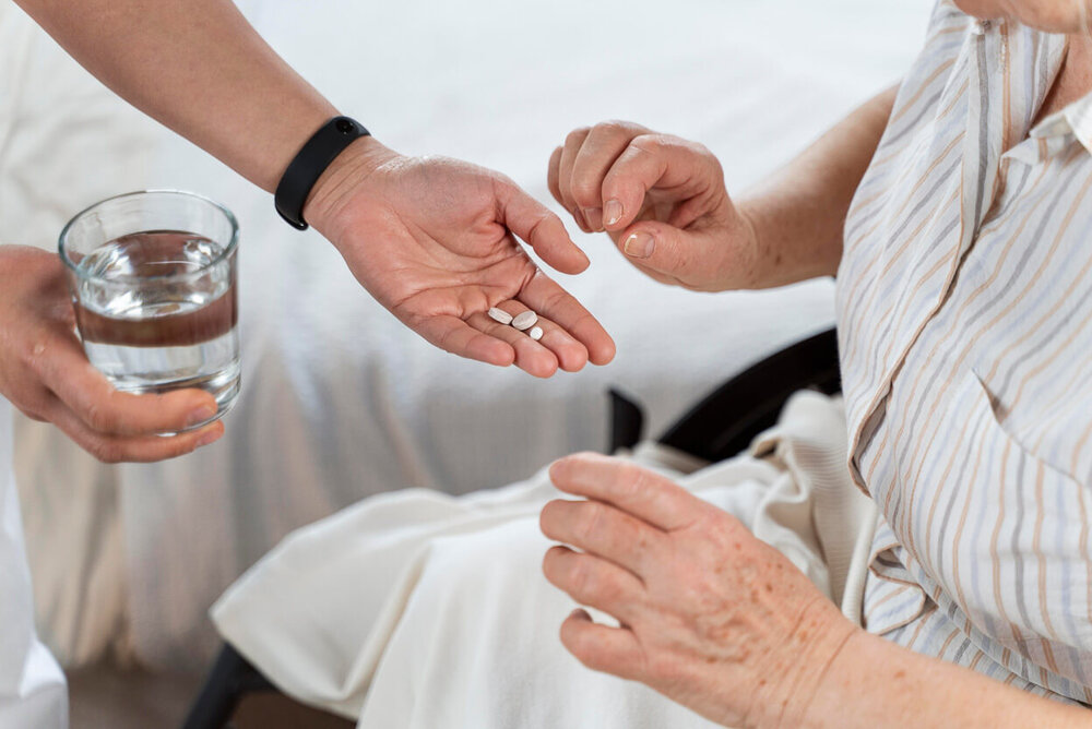 In einer Hand sind Medikamente und ein Glas Wasser für eine Person