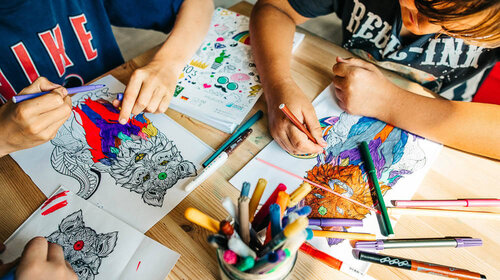 Zwei Kinder malen mit Stiften auf Papieren