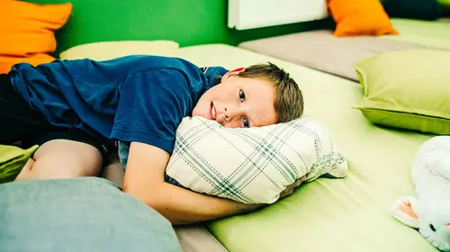 Ein junge liegt mit dem Kopf auf einem Kissen, das auf dem Boden liegt