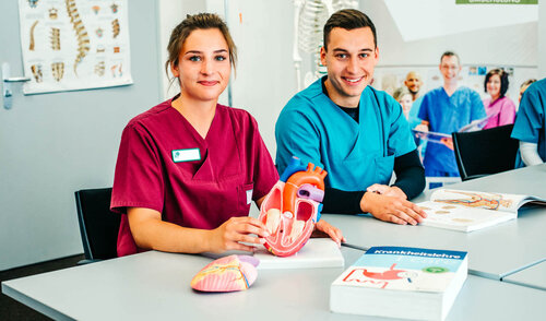Ausbildung in der Gesundheits- und Pflegeschule der Wirtschaftsakademie Nord Eine junge Frau und ein junger Mann sitzen in Dienstkleidung in der Ausbildungssituation