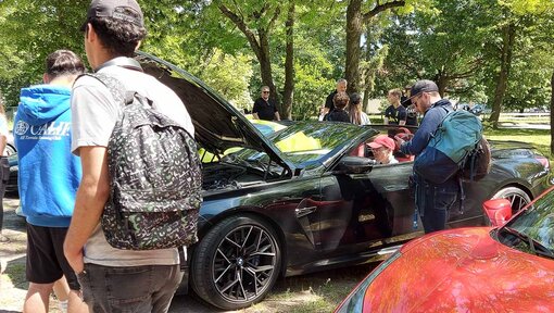 Mehrere Menschen stehen an einem Sportwagen und berühren Türen und Motorhaube