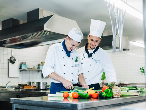 Ein Koch und ein Auszubildender schneiden Gemüse auf einem Tresen klein
