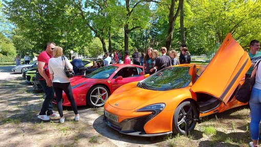 Mehrere Sportwagen stehen nebeneinander. Menschen schauen sie sich an.