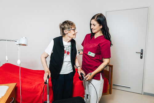 Eine Auszubildende steht bei einer älteren Dame mit Rollator