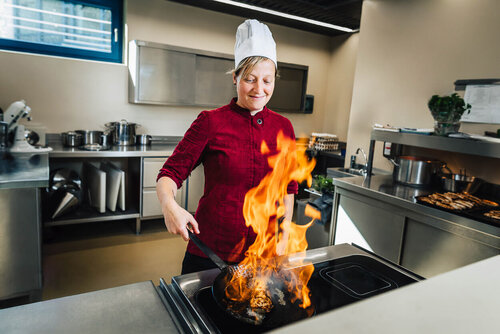 Eine junge Auszubildende schwenkt eine Pfanne mit brennendem Fett