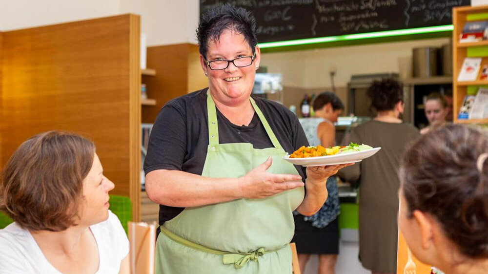 EIne Frau serviert ein Tellergericht an einem Tisch