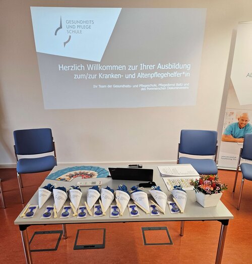 Willkommenspräsente liegen auf dem einem Tisch und eine Präsentation mit Powerpoint wird im Hintergrund angezeigt