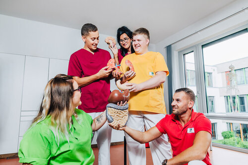 Eine Gruppe Auszubildender steht an einem Modell des menschlichen Körpers und lernt Anatomie