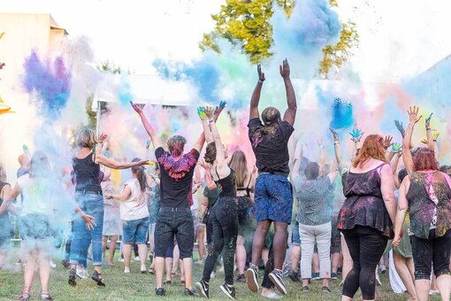 Viele jubelnde Menschen strecken die Arme in die Höhe und werfen mit Farben